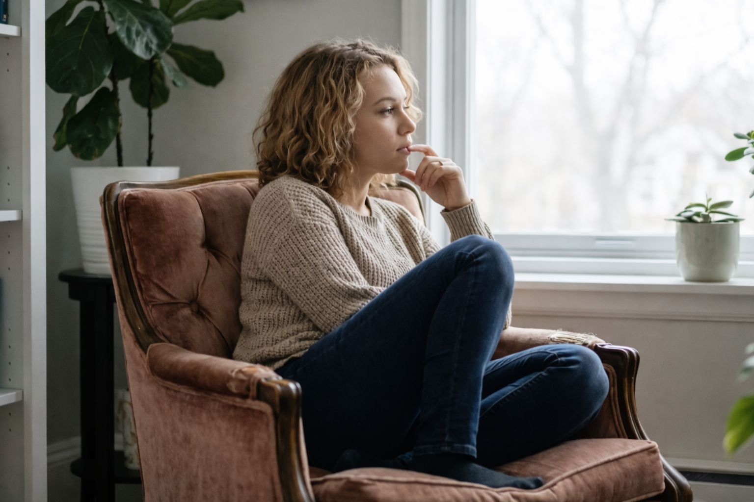 Teen sitting by a window appearing worried and reflective, symbolizing teen anxiety therapy at Watkins Counselling & Wellness in Smiths Falls.