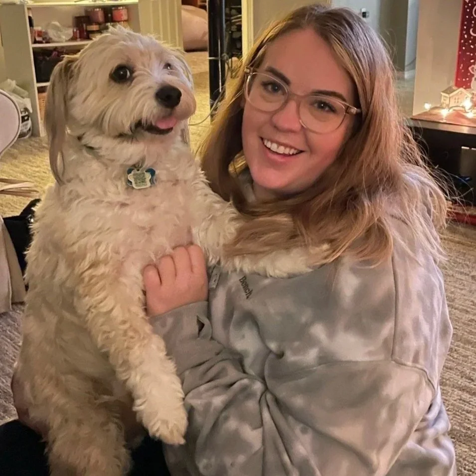 Kassandra Smalley, a young woman with glasses smiling and holding a fluffy light-colored dog with a blue collar.