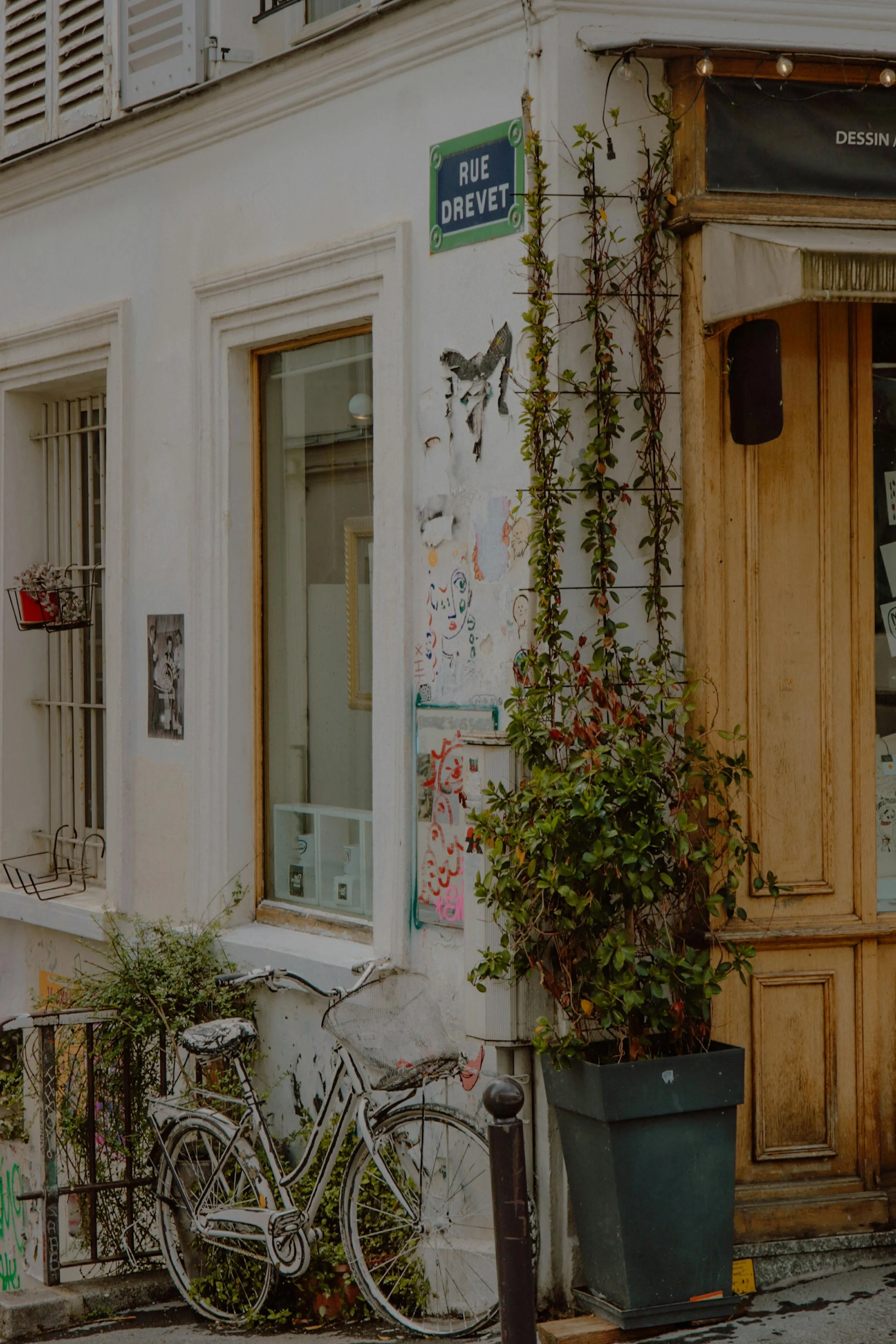 Rue Drevet à Paris avec une façade blanche, une fenêtre, une bicyclette abandonnée, une plante en pot, et des affiches d'art urbain sur le mur.