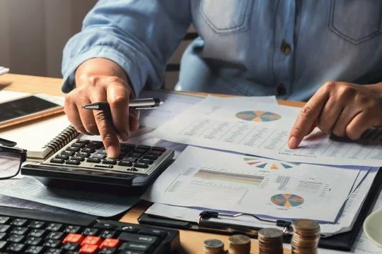 Person working with financial documents, calculator, and coins on a desk.