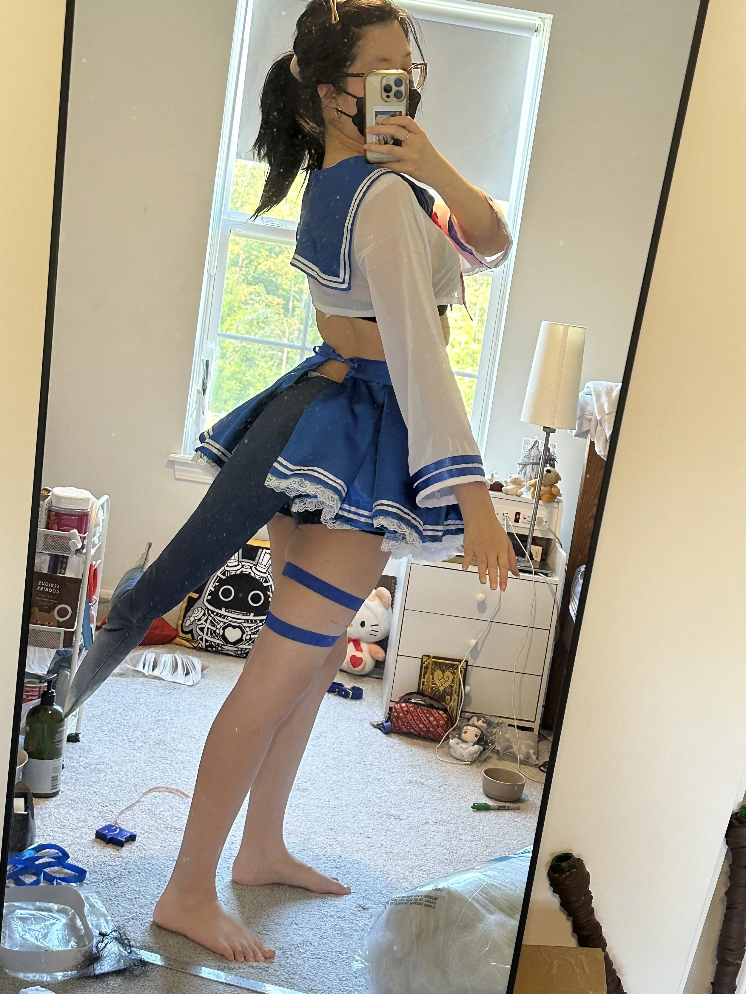 A person taking a mirror selfie in a room, dressed in a blue and white cosplay outfit with thigh-high stockings.