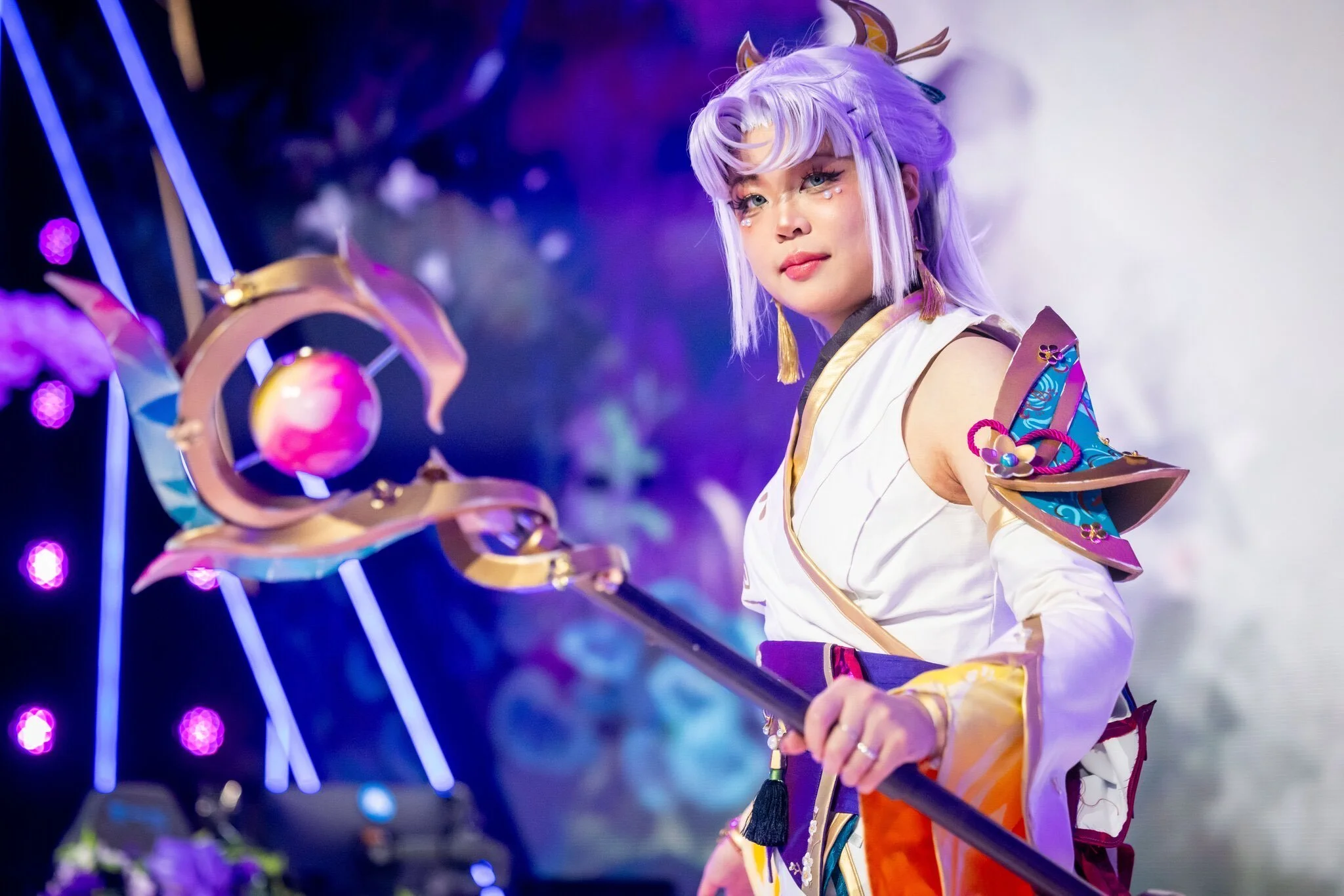 A person dressed in an elaborate fantasy costume with a staff, standing against a colorful, illuminated background.