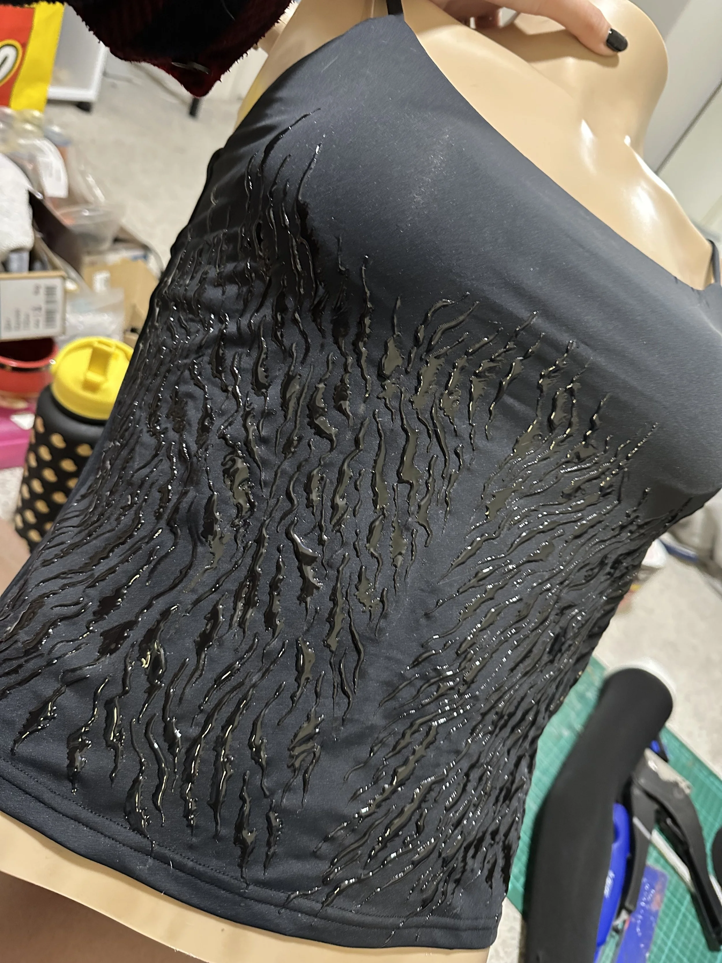 Black fabric with a pattern of wavy, shiny black lines, draped over a mannequin torso.