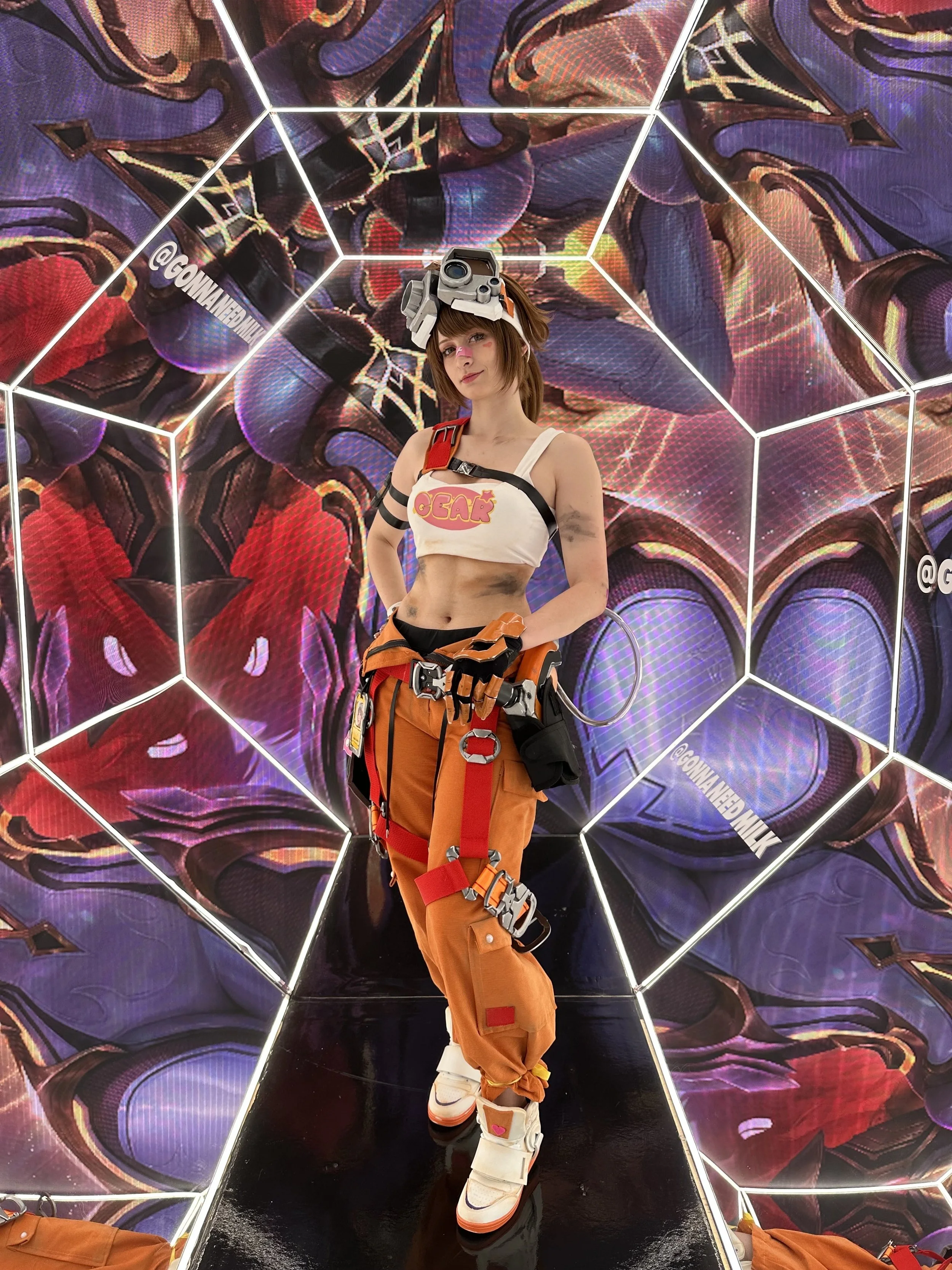 A woman dressed in futuristic climbing gear, standing inside a geometric neon-lit chamber with a vibrant, abstract digital background.