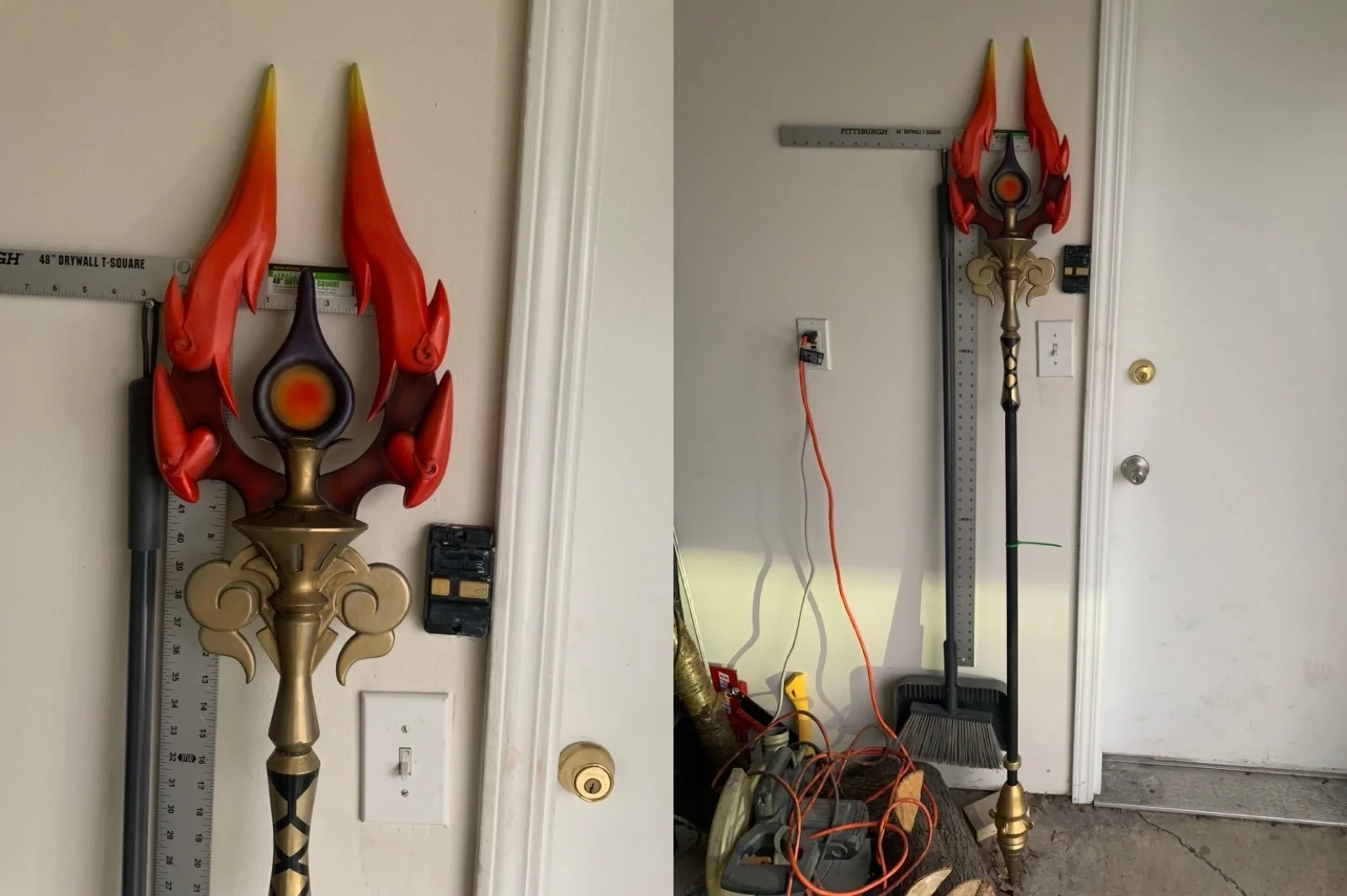 A large decorative toy weapon resembling a fantasy staff or spear, with fiery red and purple flame-like elements and a gold and black handle, leaning against a wall in a garage with electric tools and wires nearby.