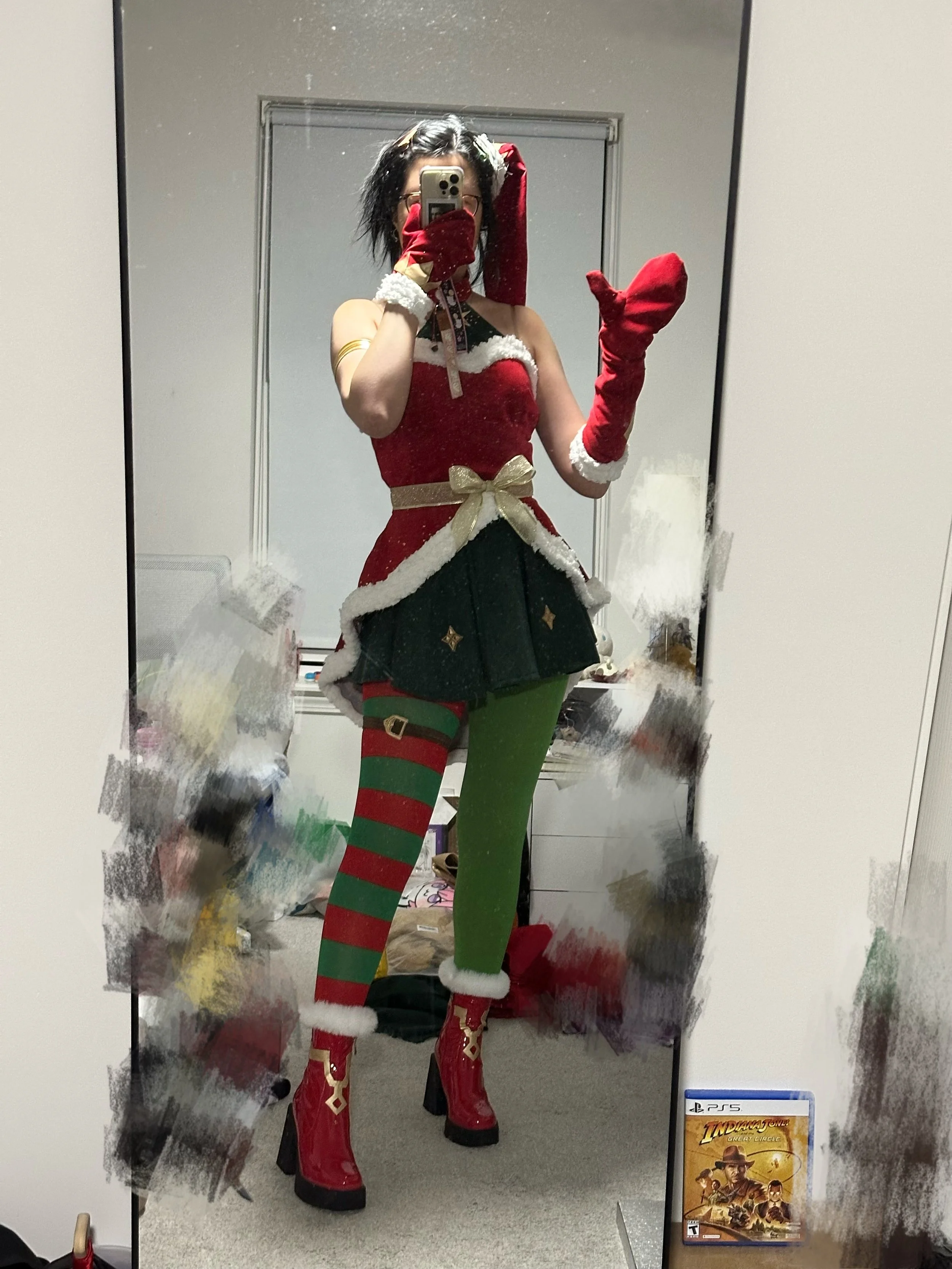 Person in a Christmas-themed costume with a red and green outfit, striped stockings, red boots, and a Santa hat, taking a selfie in a mirror.