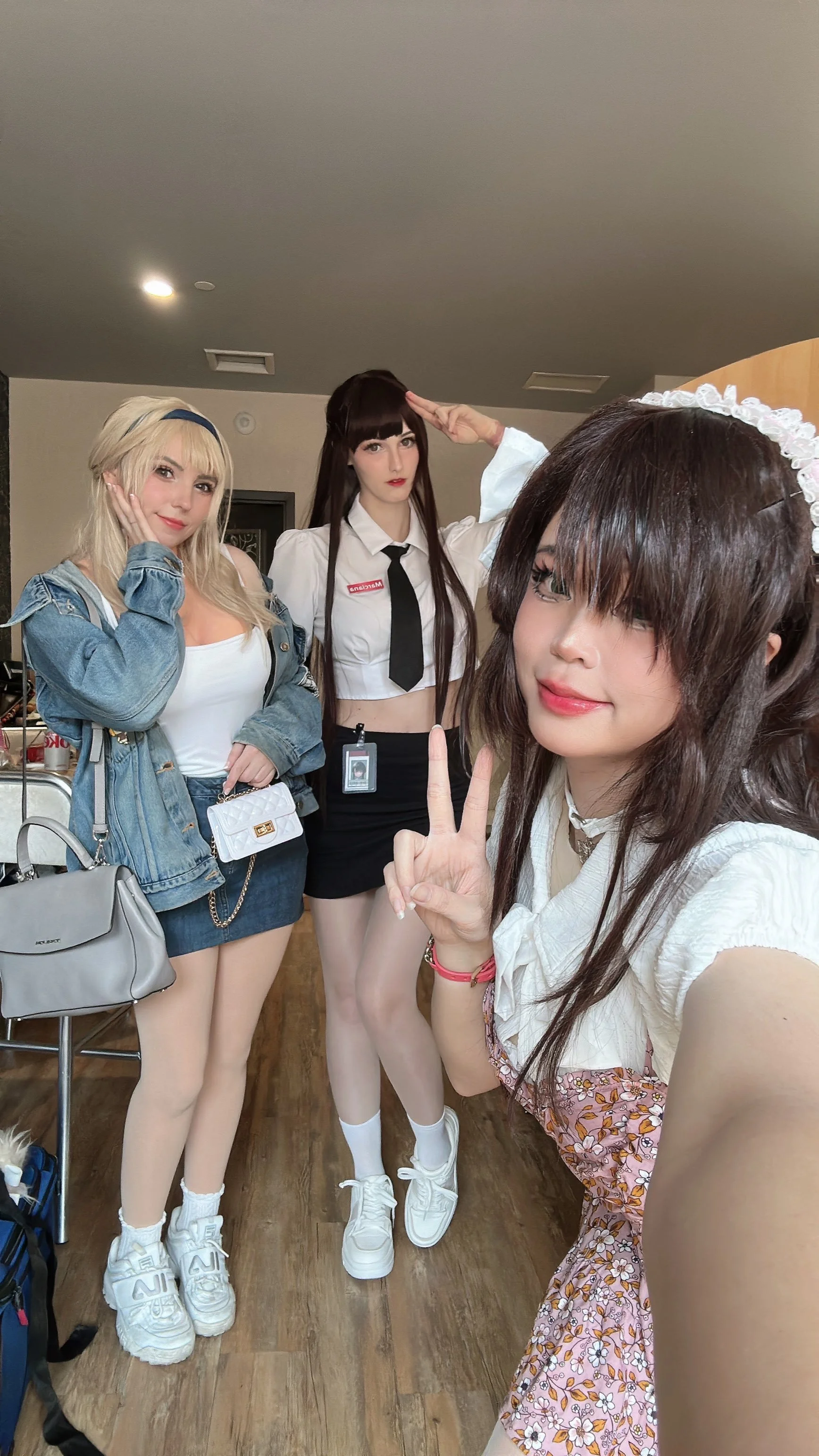 Three young women dressed in casual and cosplay outfits posing indoors, with one taking a selfie.