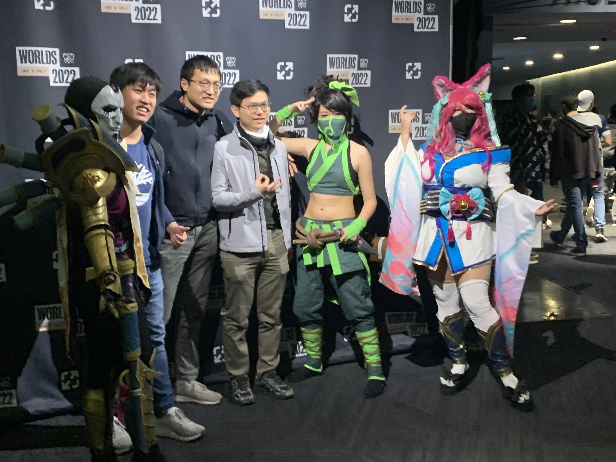 Group of five people in cosplay costumes and two in casual clothing posing together at a convention, with a backdrop displaying 'Overwatch World Cup 2022' logos.