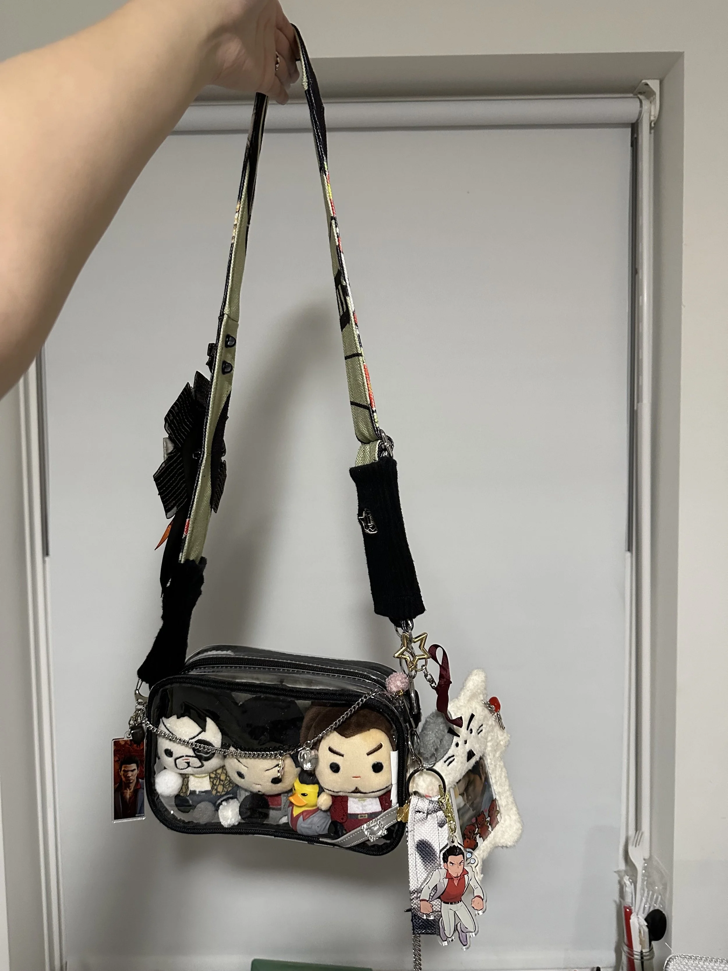 A person holding a decorative bag with plush toys and keychains hanging from it, hanging on a hook near a white door.