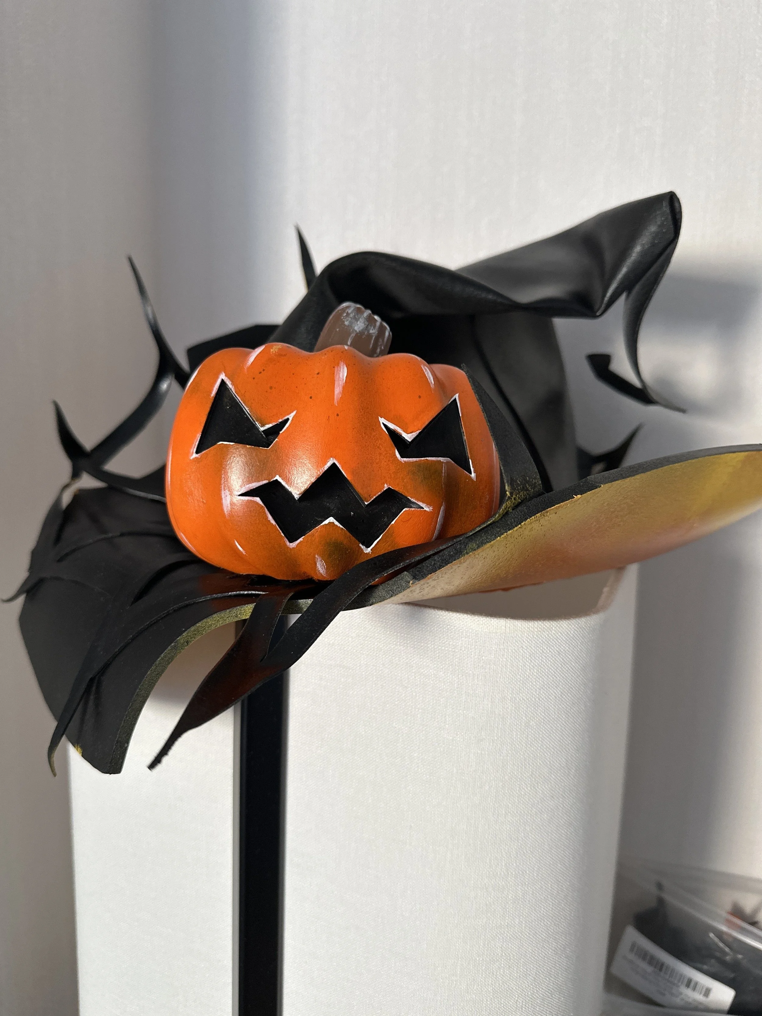 A Halloween decoration featuring a small orange pumpkin with a carved face, placed on a black paper or plastic spider web decoration.