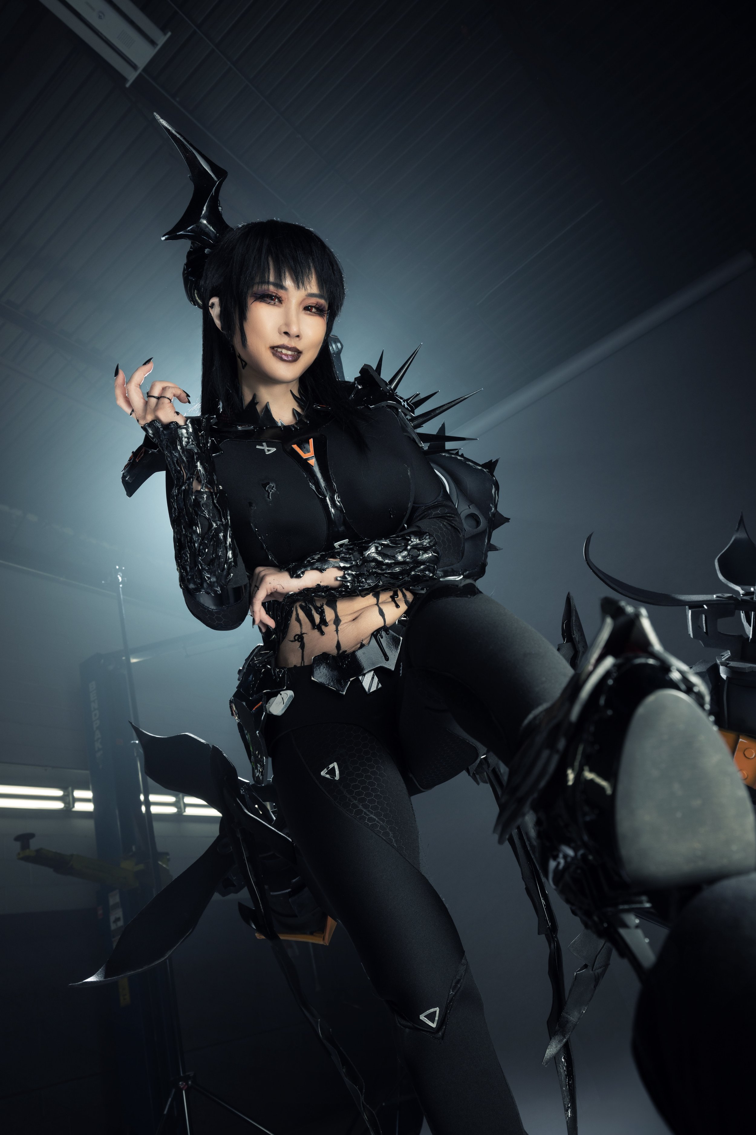 Person dressed in dark, spiked armor with a fantasy or sci-fi theme, standing inside a industrial or garage-like setting.