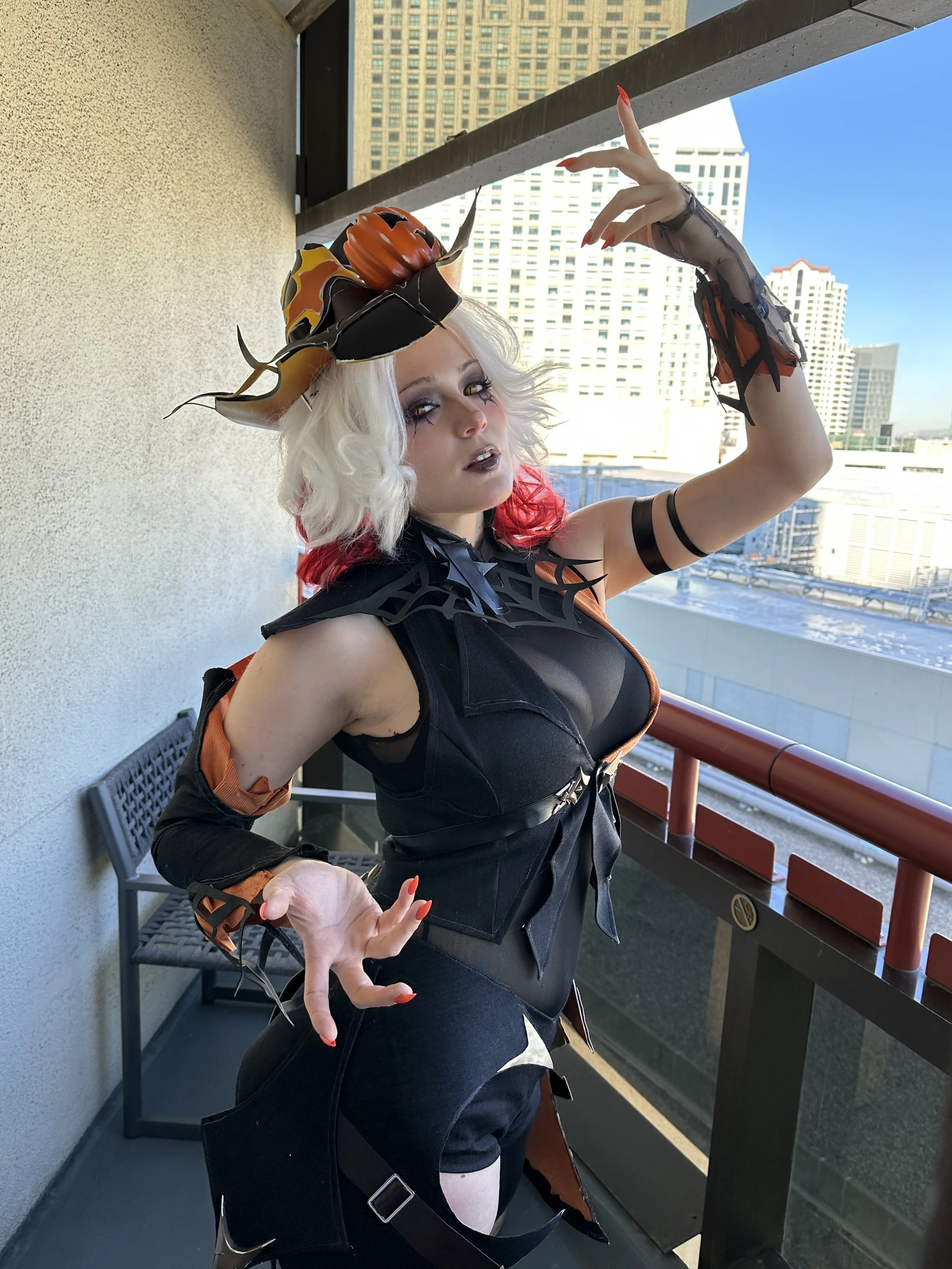 Cosplaying woman dressed as a Halloween witch or demon on balcony with city skyline in the background.