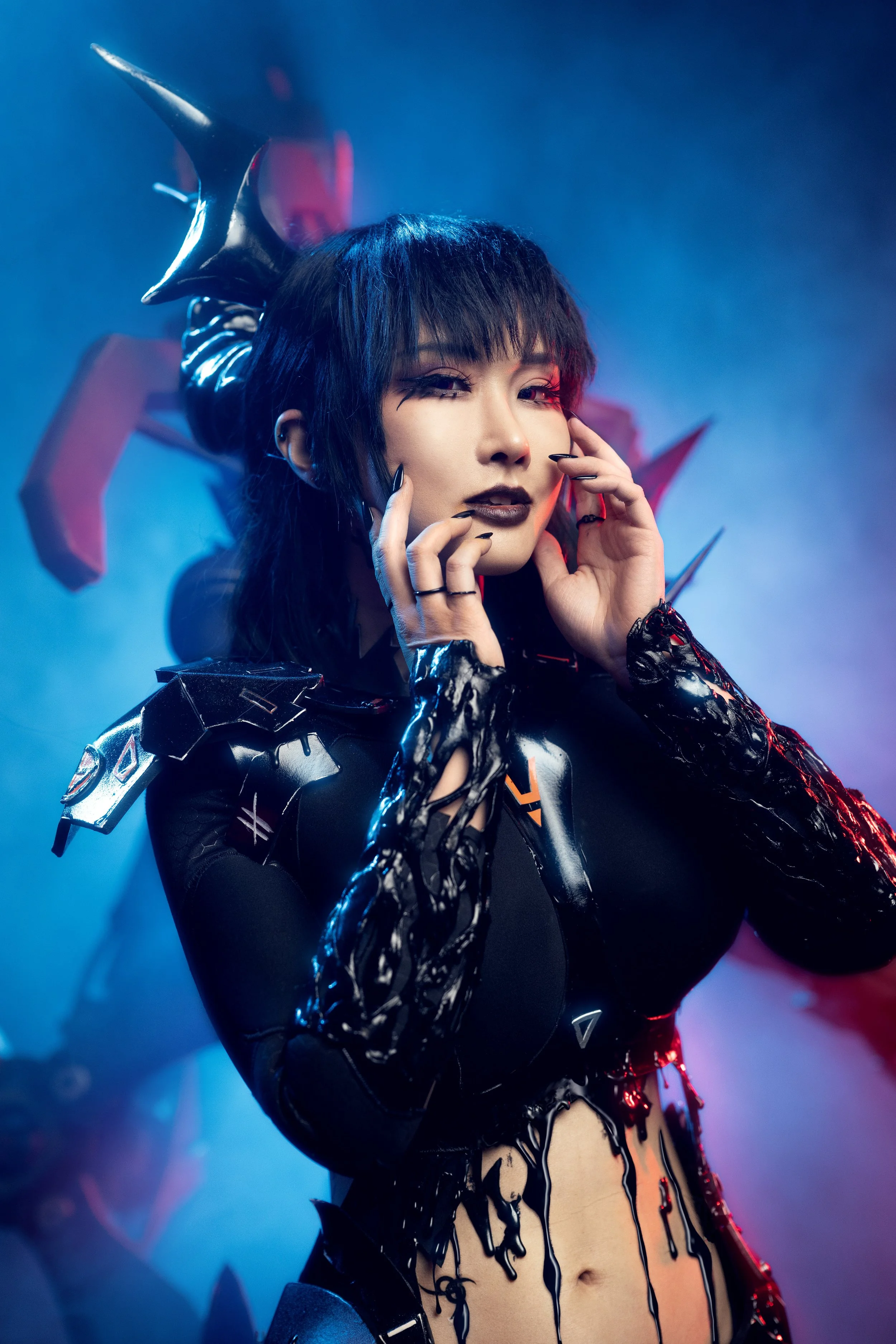 A woman in futuristic black clothing with metallic and shiny details, makeup, and accessories, posing with a smoky, colorful background.