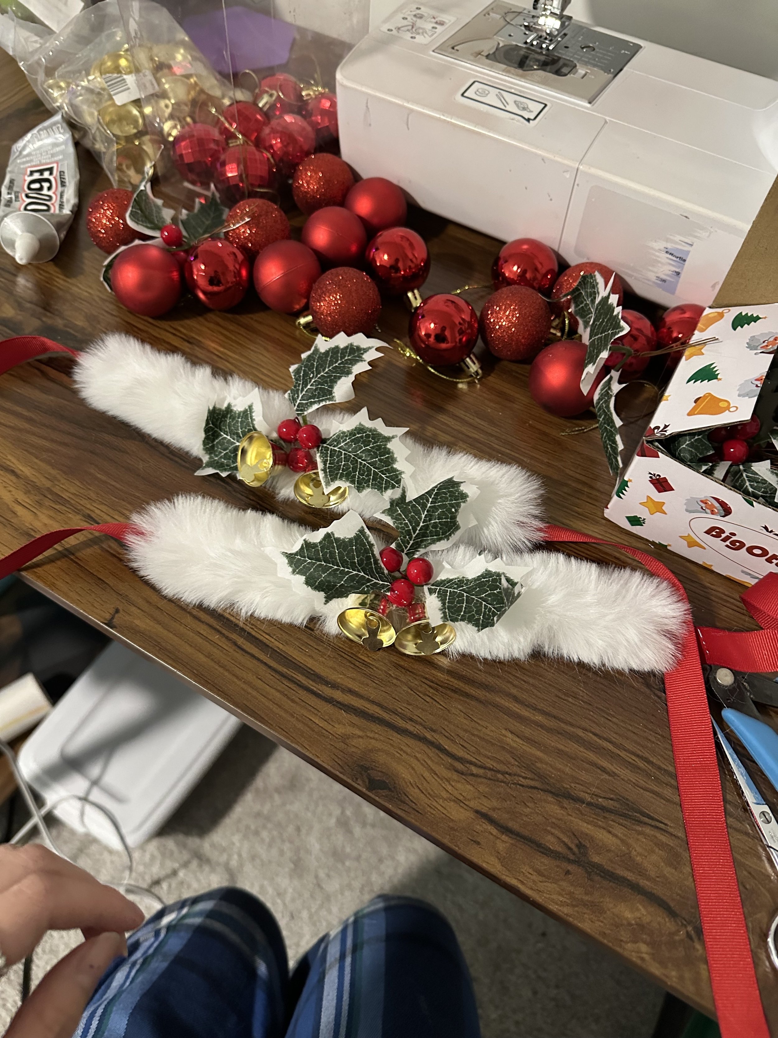 Christmas decorations on a table, including red and gold baubles, faux fur and holly leaf embellishments, and a box of assorted holiday-themed items.