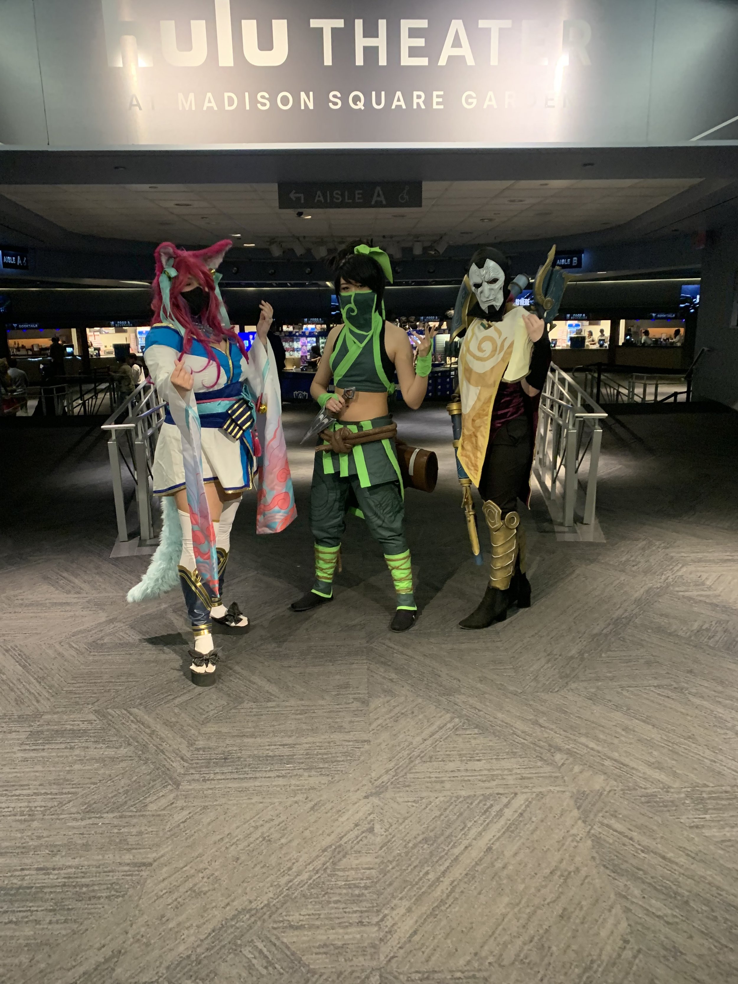 Three people in cosplay costumes standing in front of a theater sign at a convention.