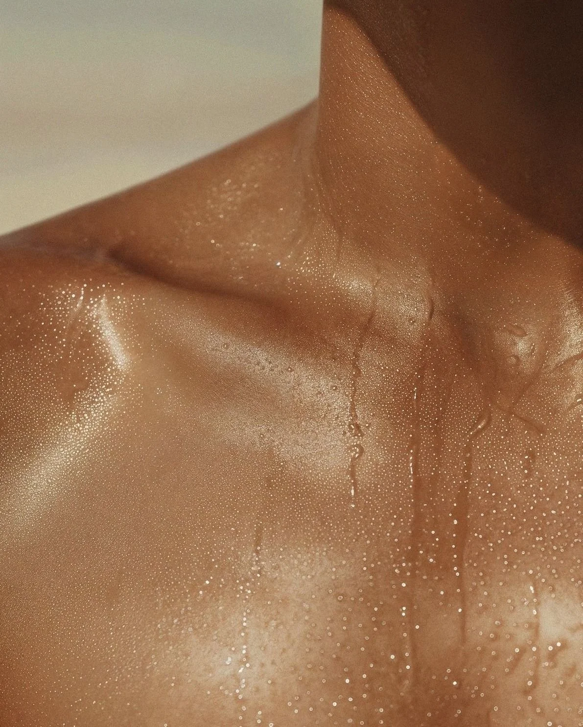 Close-up of a person's neck and shoulder with water droplets on the skin, showing a glistening, shiny appearance.
