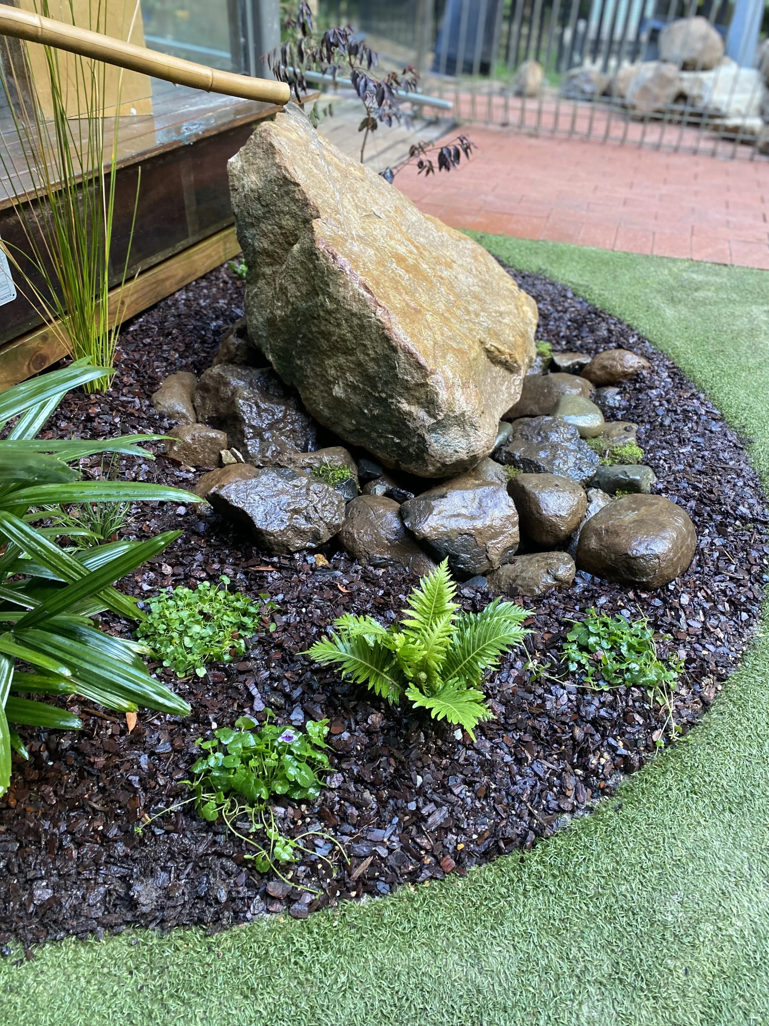 Custom water feature at Bangalow Community Children’s Centre, featuring a natural stone pond with gentle flow, surrounded by native planting and designed to create a calming focal point in the Northern Rivers garden
