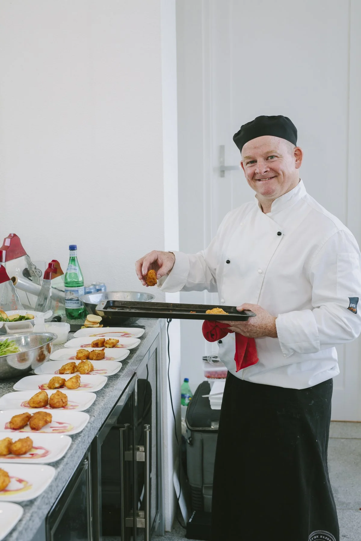 A chef in a white uniform and black hat serving fried food onto plates on a kitchen counter.