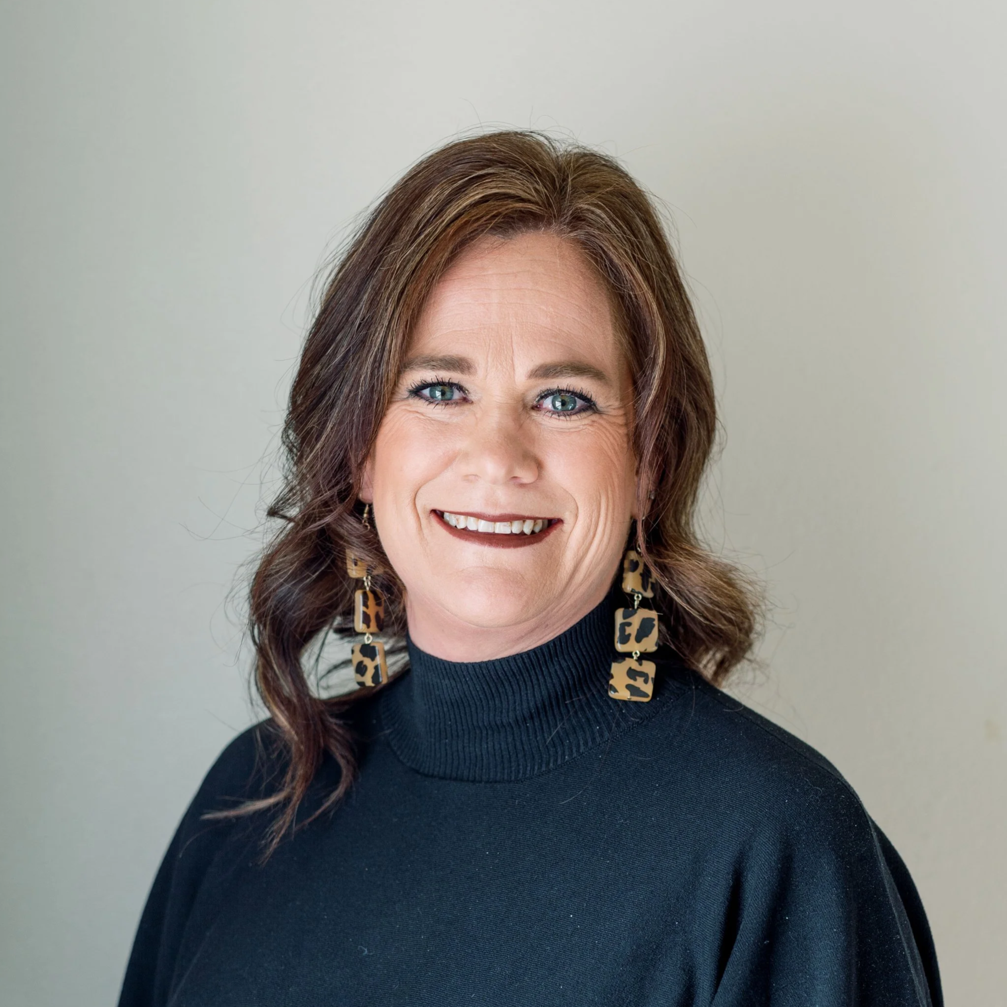 Headshot of Jamie Poe in a black sweater with tortoise shell earrings
