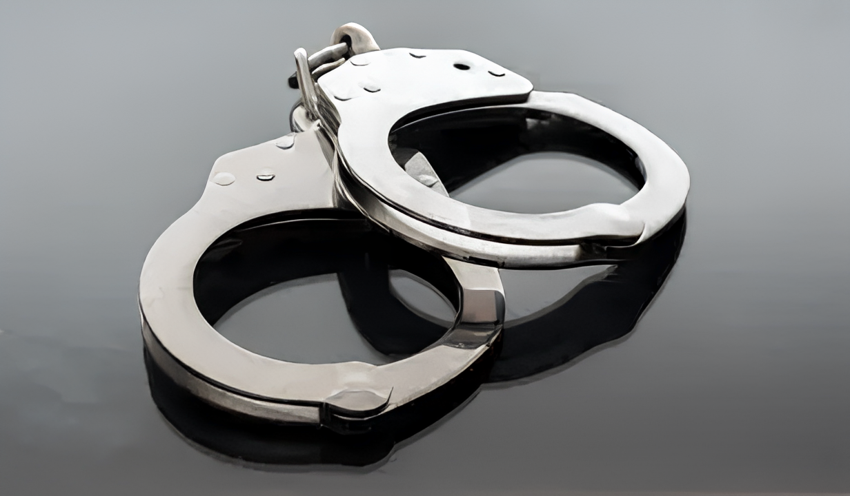 A pair of silver metal handcuffs on a reflective dark surface.