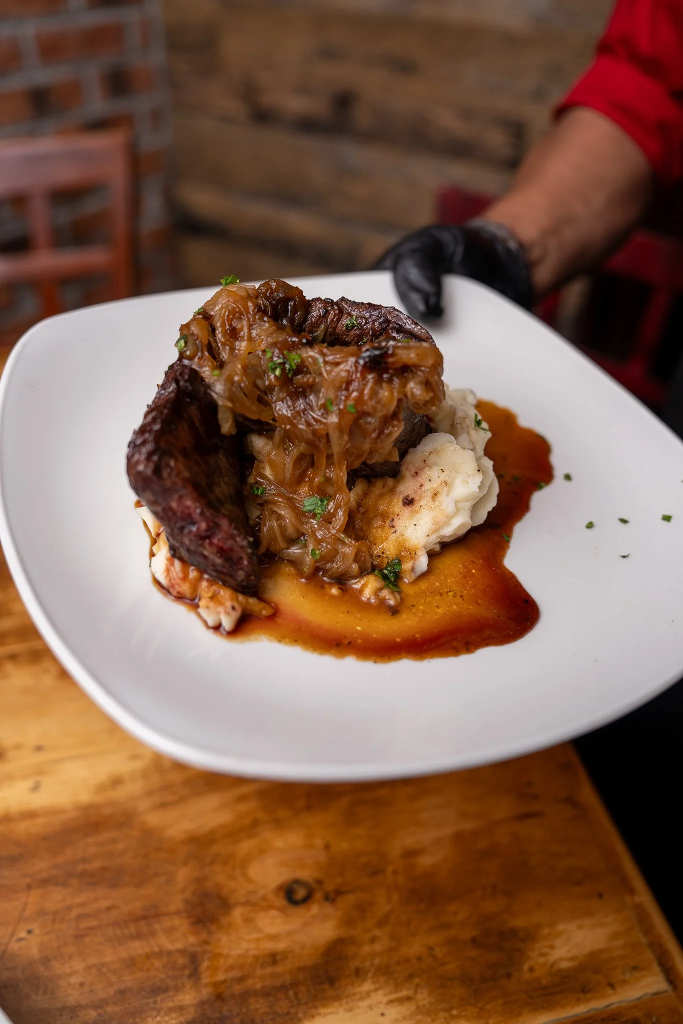 A plate of mashed potatoes topped with pot roast, caramelized onions, and gravy, served on a white plate.