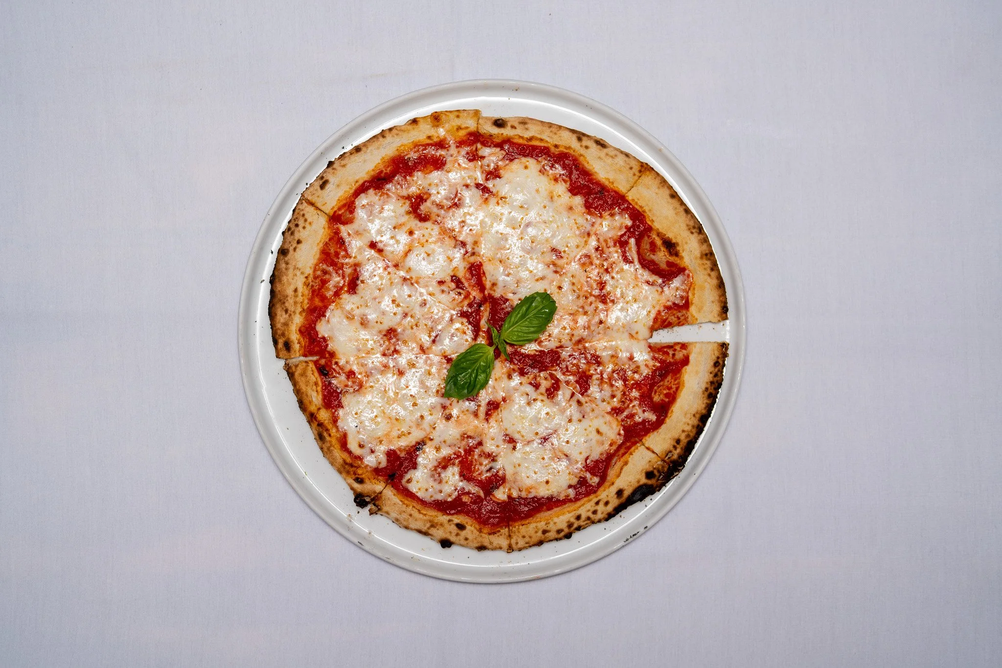 A cheese pizza garnished with basil leaves on a white plate against a white background.