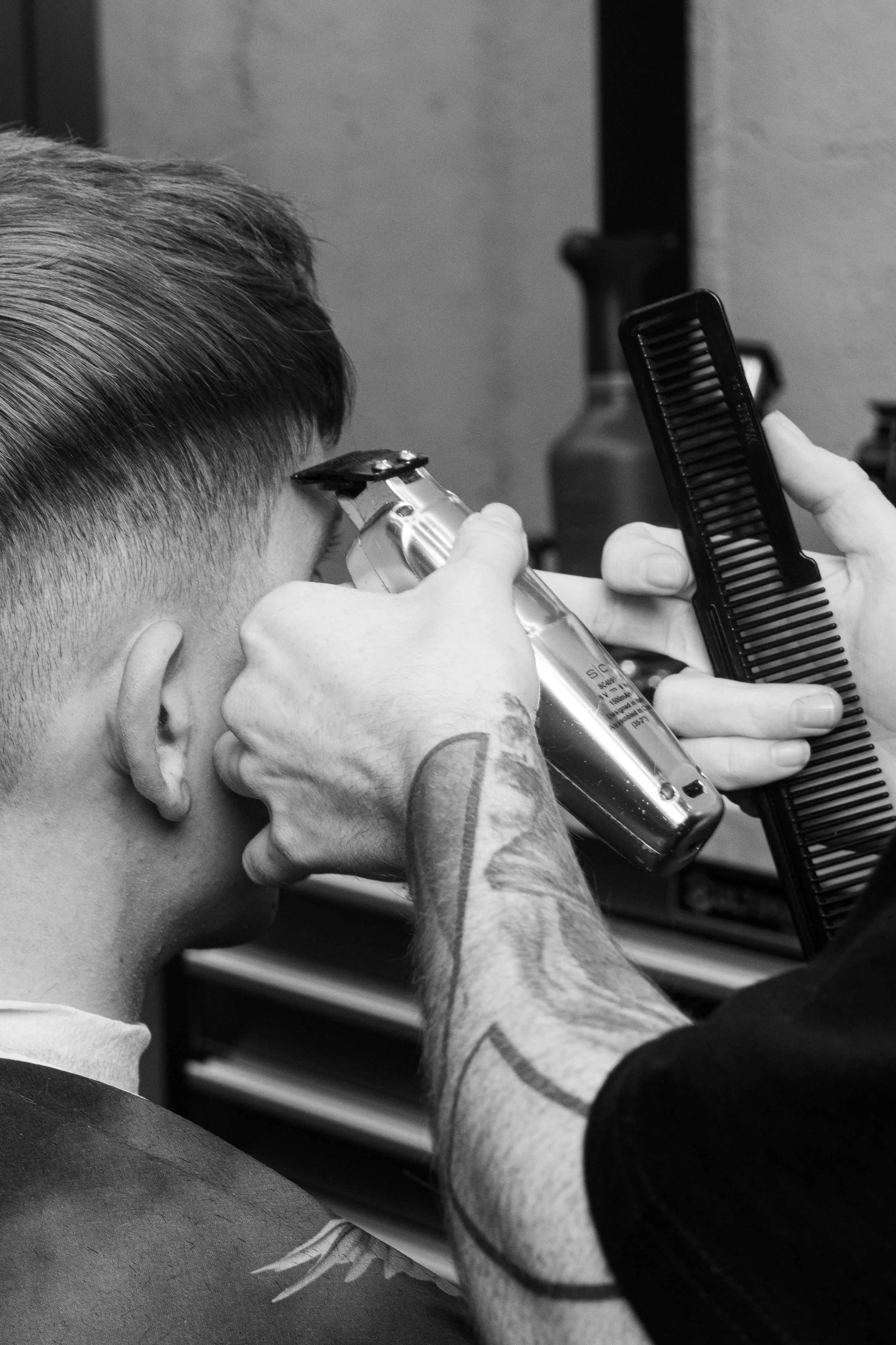 A person getting a haircut, with a barber using clippers and a comb, in black and white.