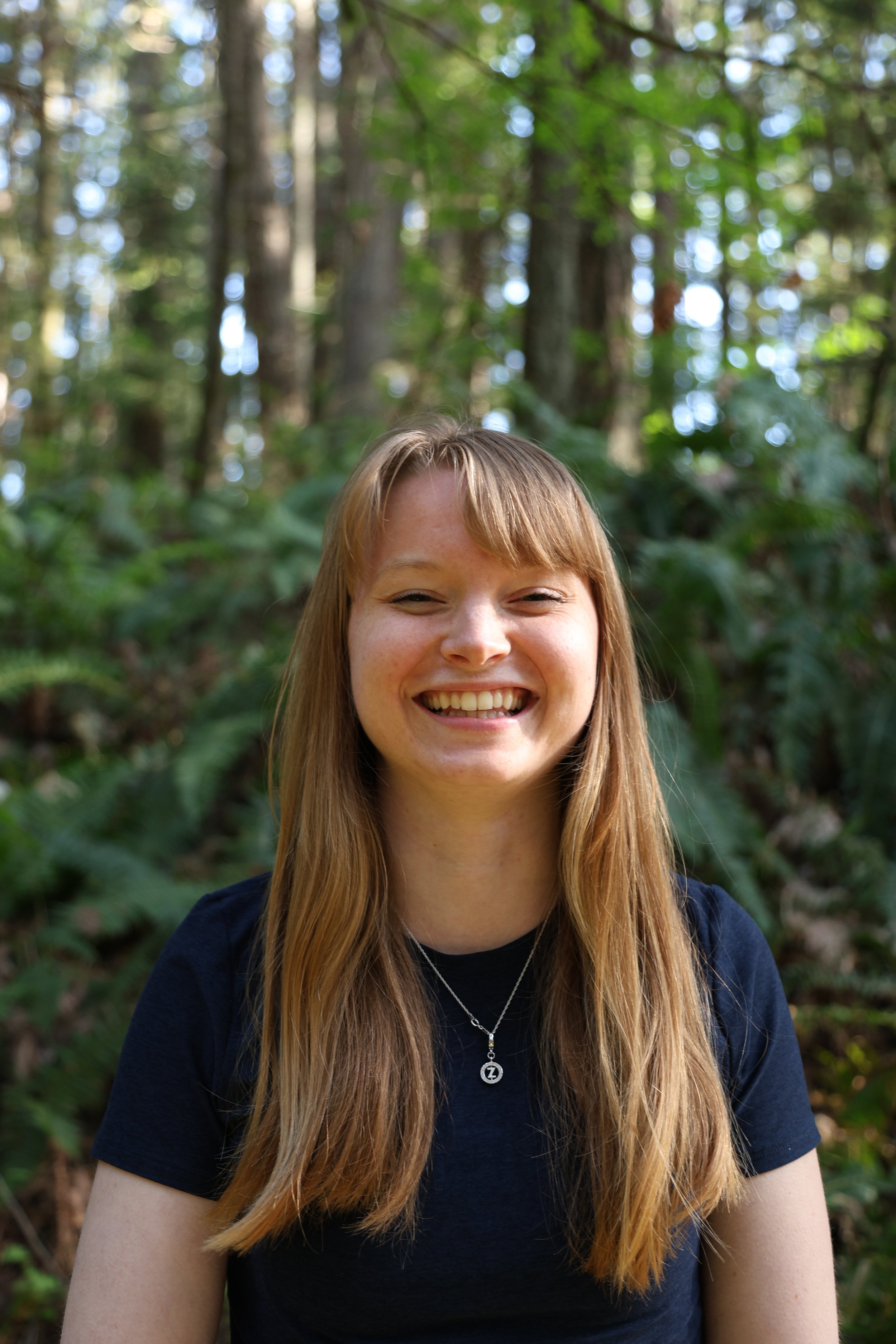 A young woman, founder of Prana Path Yoga, Zoya,  smiling in a lush green forest.