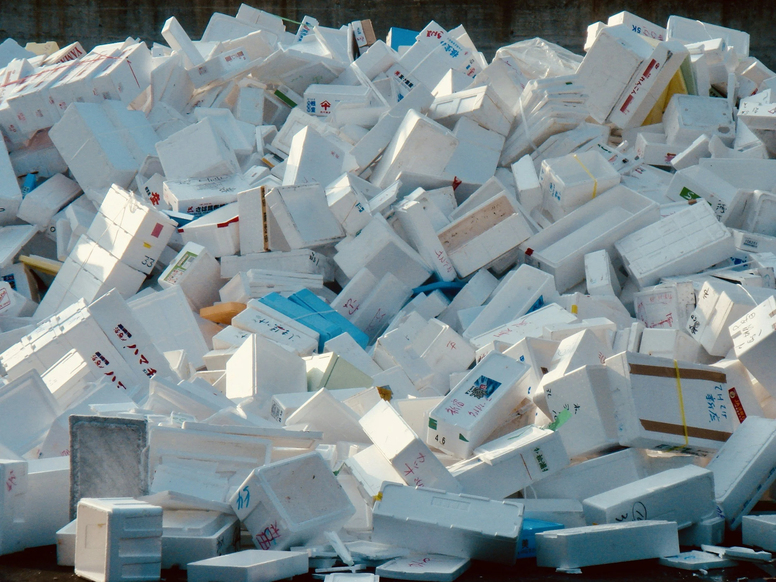 Large pile of discarded foam food containers, mostly white with some colored and labeled with Japanese characters, outdoors.