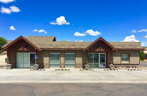 A commercial building with a gray roof, beige siding, and large glass windows. There is a handicapped parking sign and space in front of the building, with a blue sky and a few clouds above.