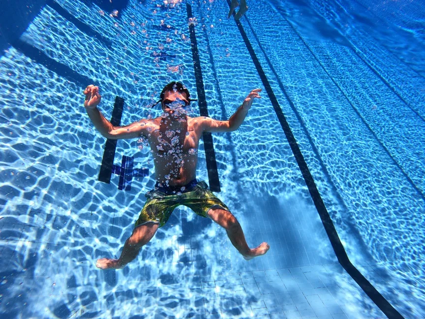 Child with swim goggles and swim trunks underwater in a swimming pool.