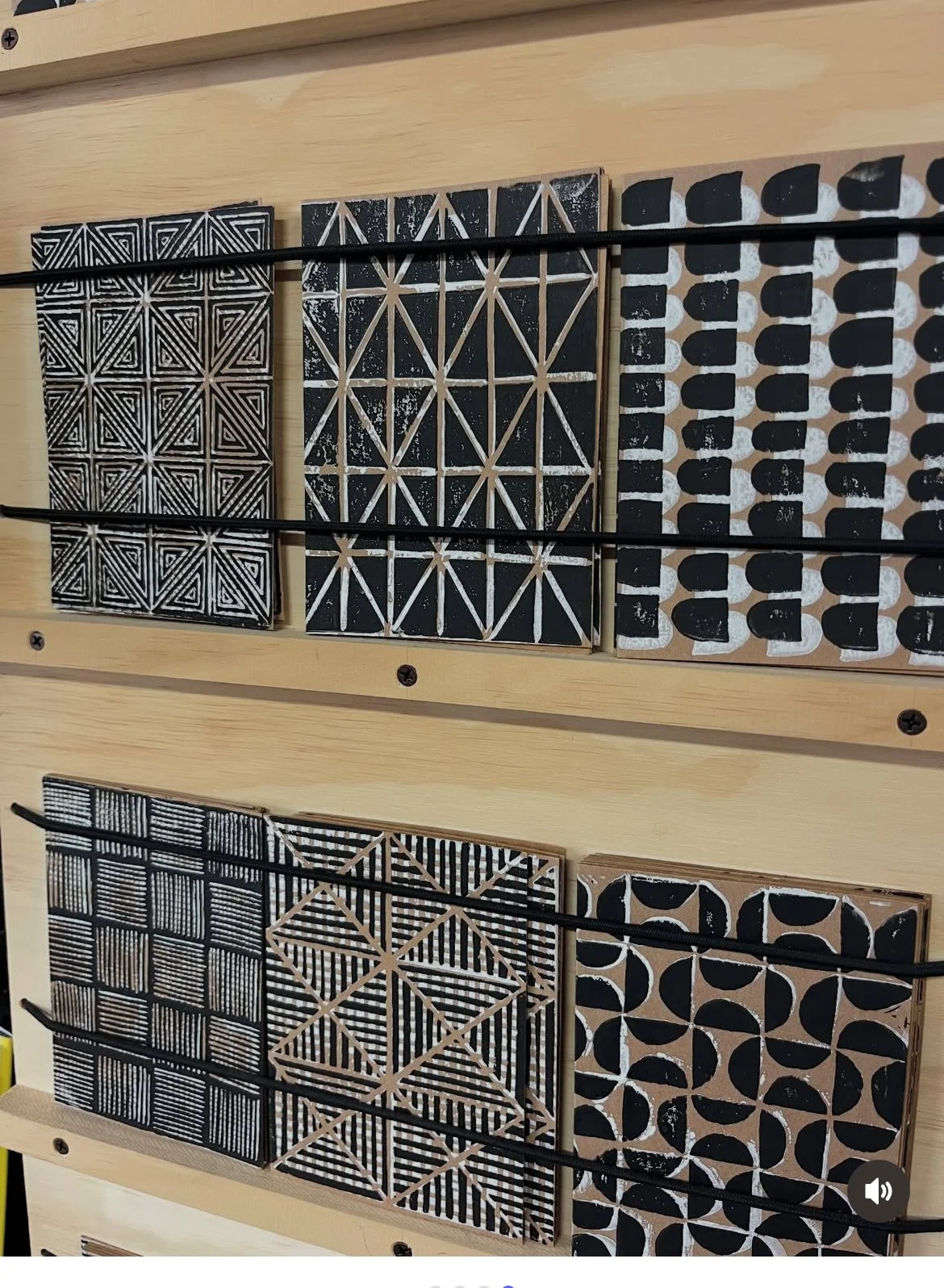 Two rows of six black and natural wood tiles with geometric black and white patterns, mounted on a light wooden surface.