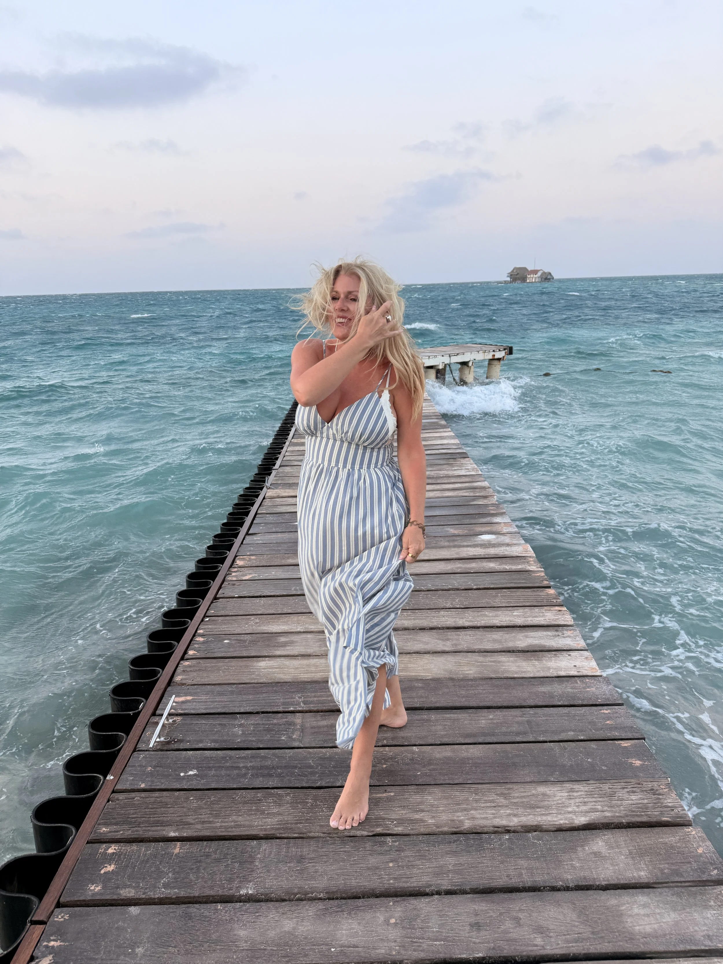 Shayla Menzie walking barefoot on a wooden pier overlooking the Caribbean Sea.