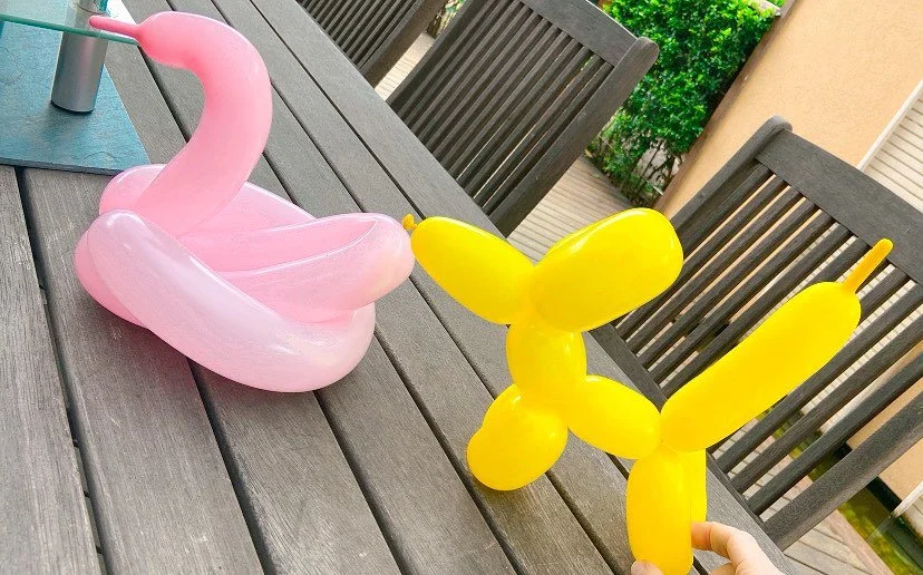 Two inflatable balloon sculptures of a pink swan and a yellow dog placed on an outdoor wooden table.