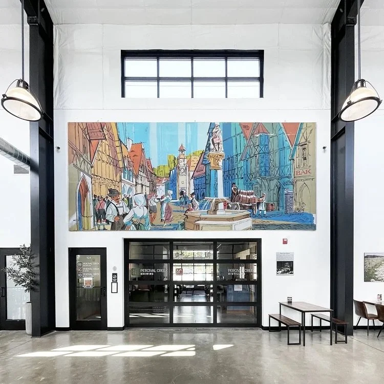 Large colorful painting of a European town square with buildings, a clock tower, statues, and people, mounted on a white wall behind a glass entrance door.