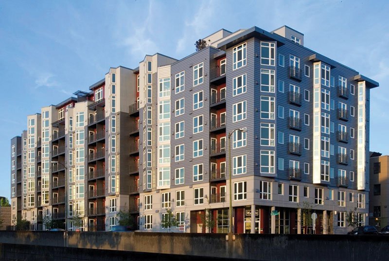 Modern kitchen with white cabinets, black hardware, stainless steel appliances, and light wood flooring, featuring a loft area with a wooden ladder.