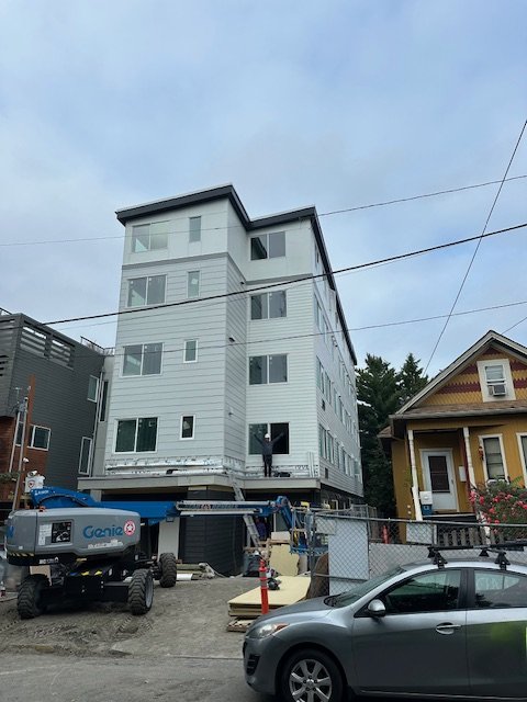 Interior of a modern restaurant with tables, chairs, and booth seating, brick walls, large windows, and contemporary lighting fixtures.