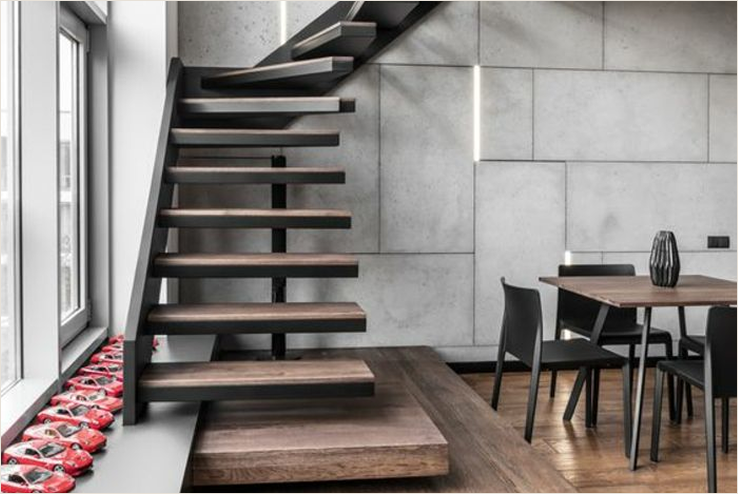 A modern building with a metal siding, brick accents, and large windows, featuring a fish decoration on the left window and a sign indicating it is a wine bar and shop, located along a street with visible utility poles and trees.