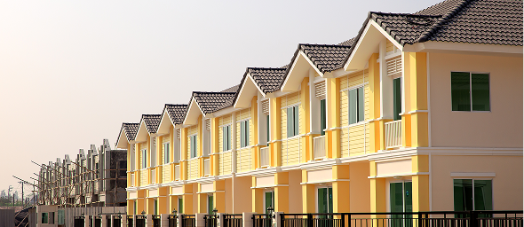 Front view of a modern two-story house painted dark gray with large windows, a garage, and a landscaped front yard with small bushes, flowers, rocks, and a concrete walkway.