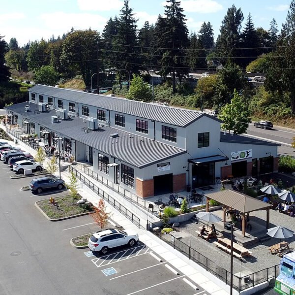 A modern building with a metal siding, brick accents, and large windows, featuring a fish decoration on the left window and a sign indicating it is a wine bar and shop, located along a street with visible utility poles and trees.