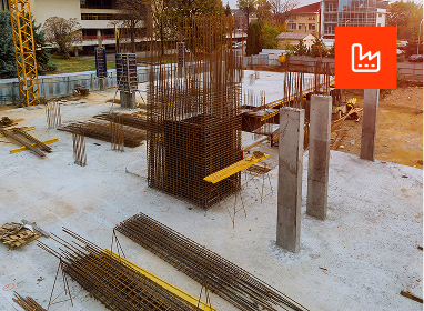 Front view of a modern two-story house painted dark gray with large windows, a garage, and a landscaped front yard with small bushes, flowers, rocks, and a concrete walkway.