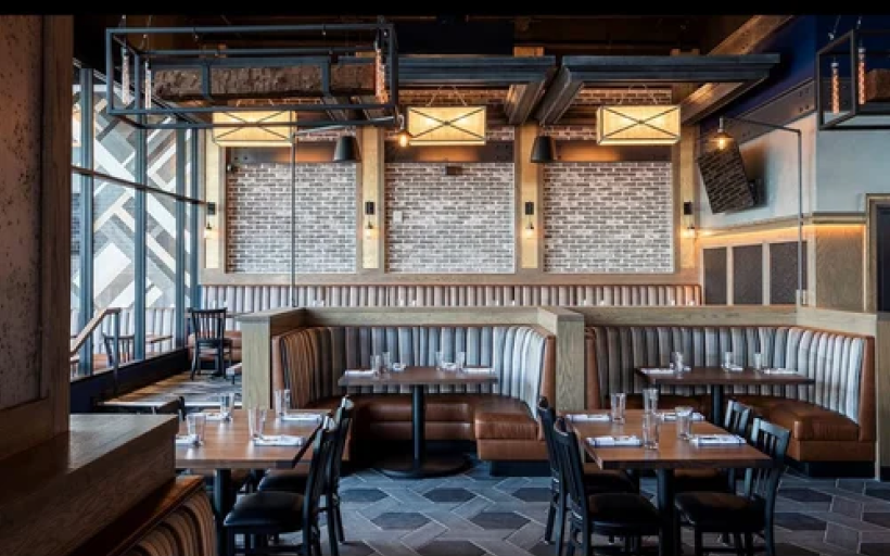 A modern building with a metal siding, brick accents, and large windows, featuring a fish decoration on the left window and a sign indicating it is a wine bar and shop, located along a street with visible utility poles and trees.