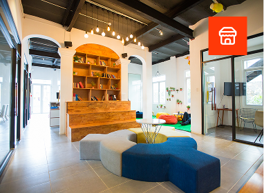 A modern building with a metal siding, brick accents, and large windows, featuring a fish decoration on the left window and a sign indicating it is a wine bar and shop, located along a street with visible utility poles and trees.