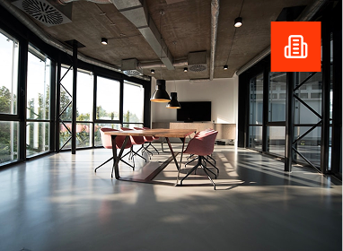 Modern kitchen with light wood cabinets, stainless steel appliances including a dishwasher, oven, and refrigerator, and a laundry area with a washing machine and dryer in the background. The room has wood-look flooring and white walls with small windows.