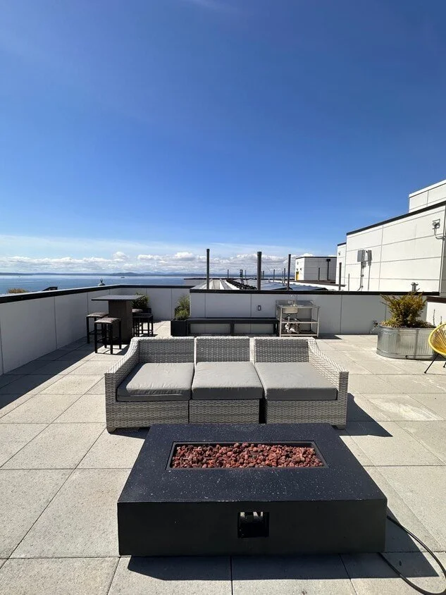 Rooftop patio with outdoor furniture, a fire pit, potted plants, and a view of the sky and clouds.