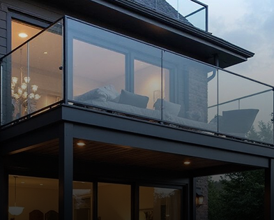 Modern kitchen with light wood cabinets, stainless steel appliances including a dishwasher, oven, and refrigerator, and a laundry area with a washing machine and dryer in the background. The room has wood-look flooring and white walls with small windows.