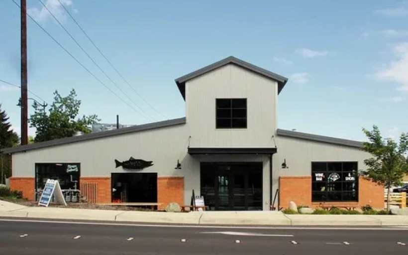 Front view of a modern two-story house painted dark gray with large windows, a garage, and a landscaped front yard with small bushes, flowers, rocks, and a concrete walkway.