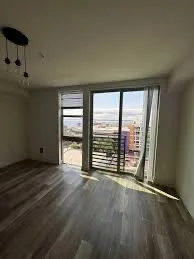 A room with large windows and balcony door, city view outside, wood flooring, and ceiling light fixture.