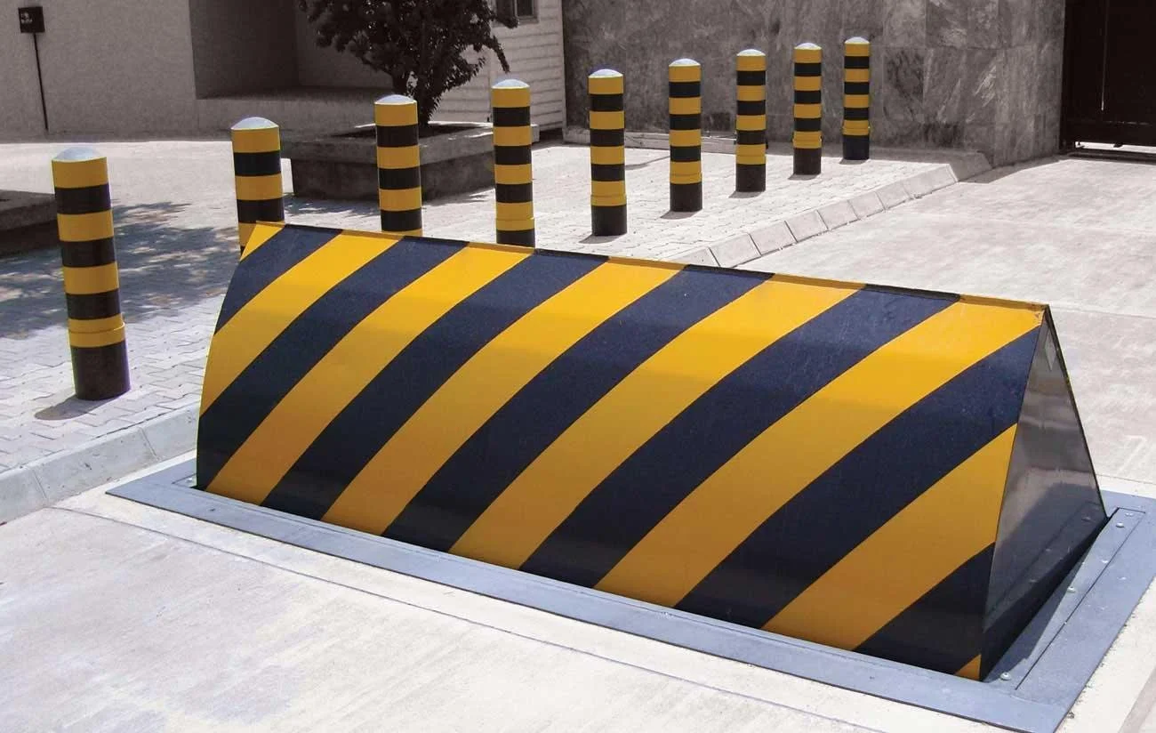 Concrete barriers on side of a paved road with a black metal fence and green trees in the background.