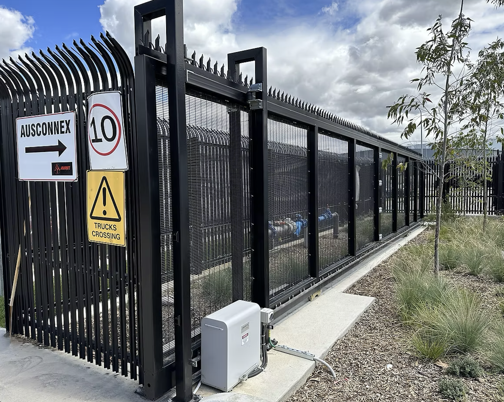 Black metal security gate in front of a gray building with closed rolling shutters